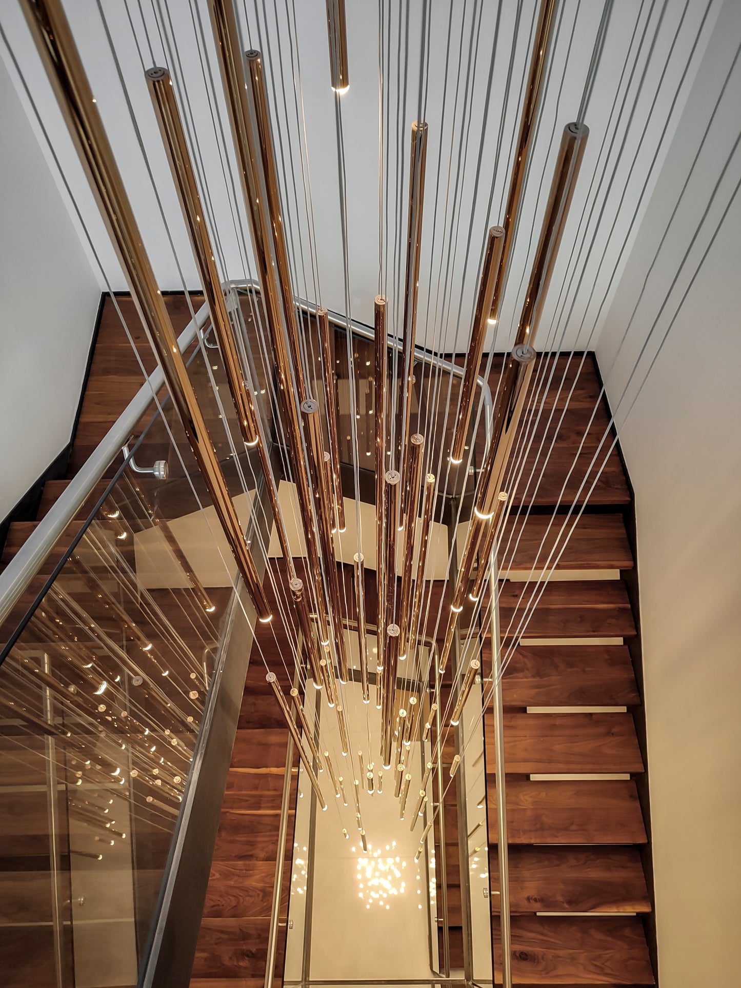 Lámpara colgante moderna de tubos dorados sobre escalera de madera, iluminación decorativa.