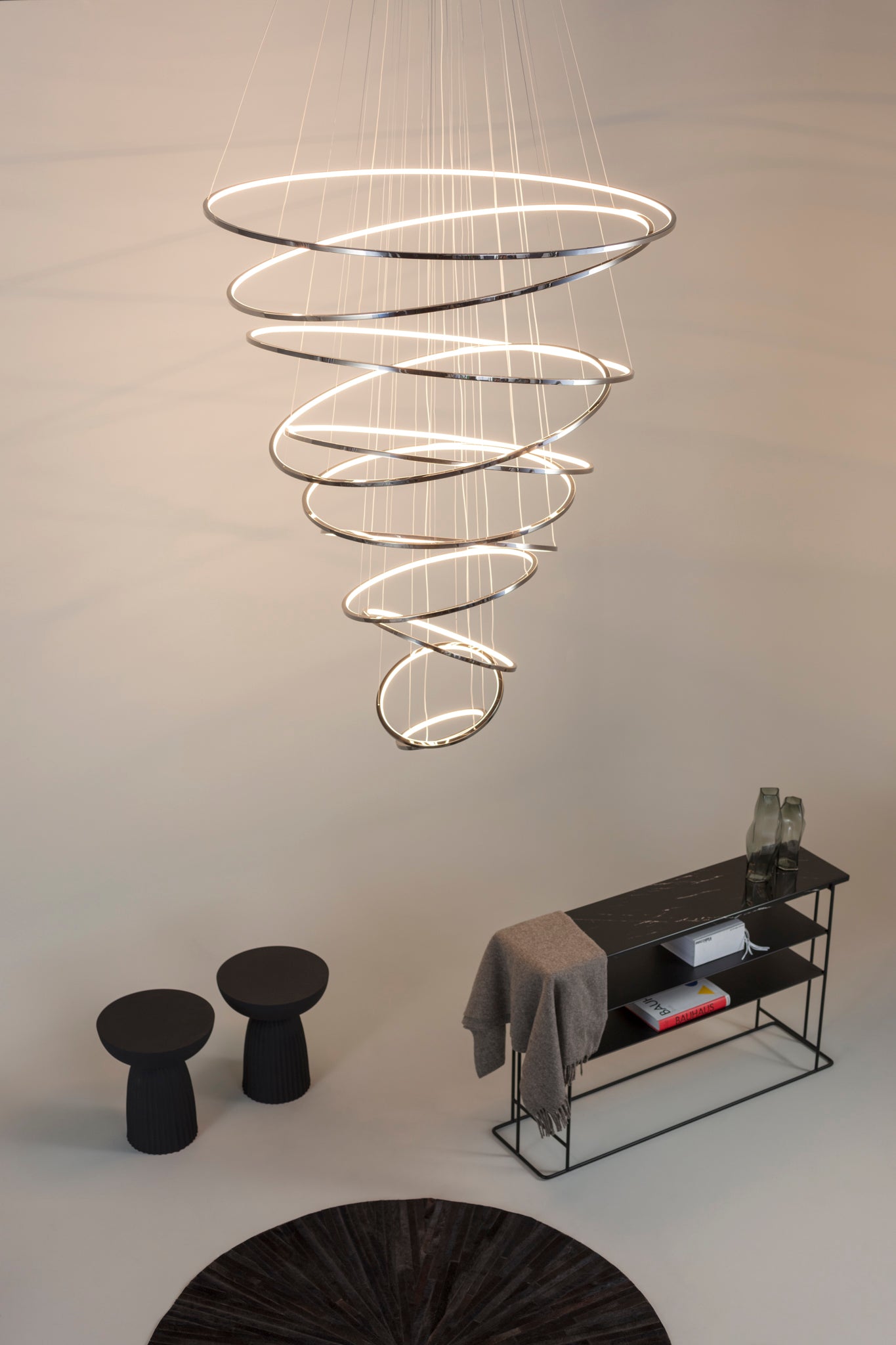 Lámpara colgante moderna de aros LED en espiral sobre mesa y taburetes en sala minimalista