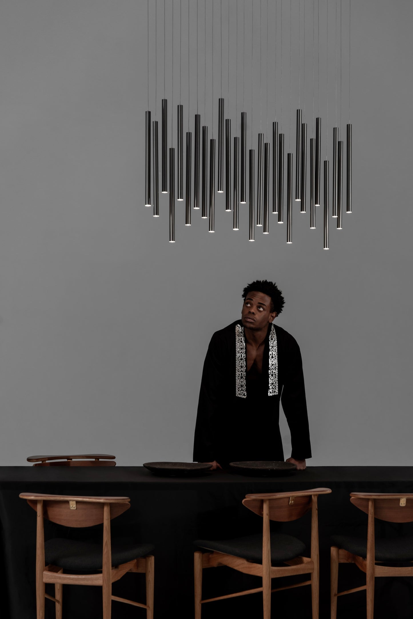 Lámpara colgante moderna negra sobre comedor minimalista con sillas de madera y hombre de pie.