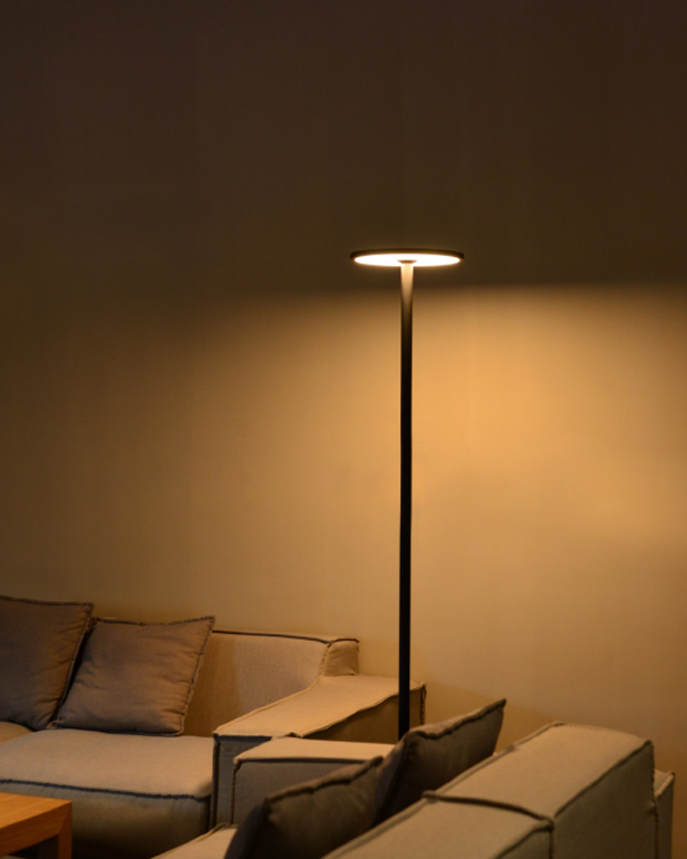 Lámpara de pie moderna encendida en sala de estar con sofá gris y luz cálida ambiental
