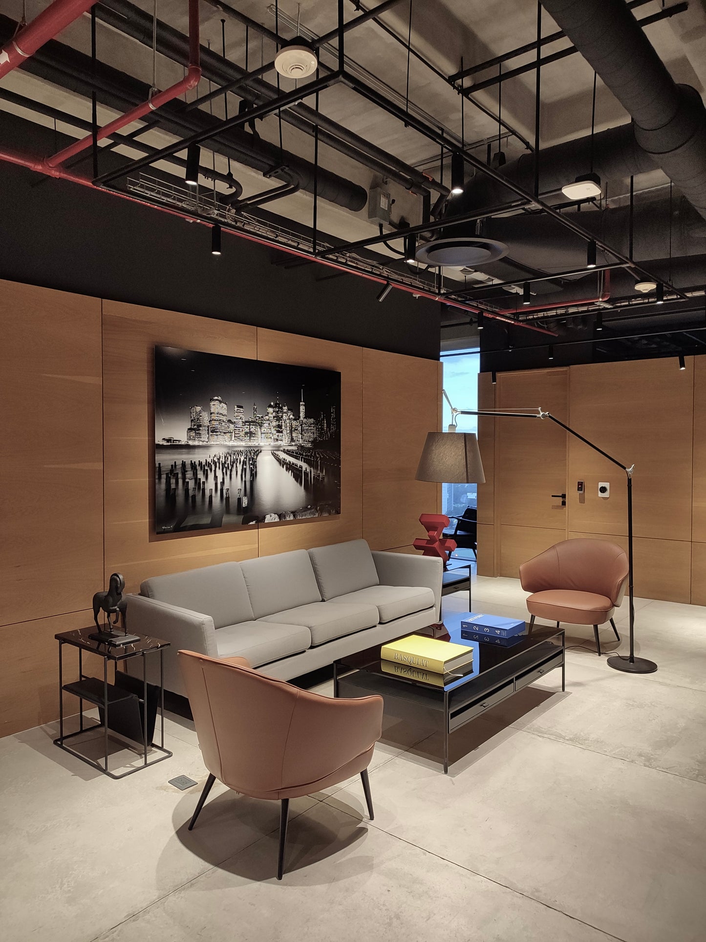 Sala moderna con sofá gris, sillones beige, mesa de centro negra y lámpara de pie, iluminación industrial.