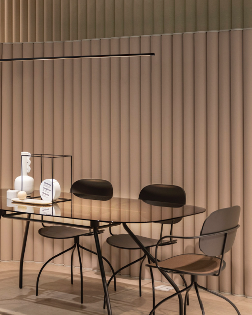 Lámpara lineal de techo moderna sobre mesa de vidrio y sillas negras, ambiente minimalista