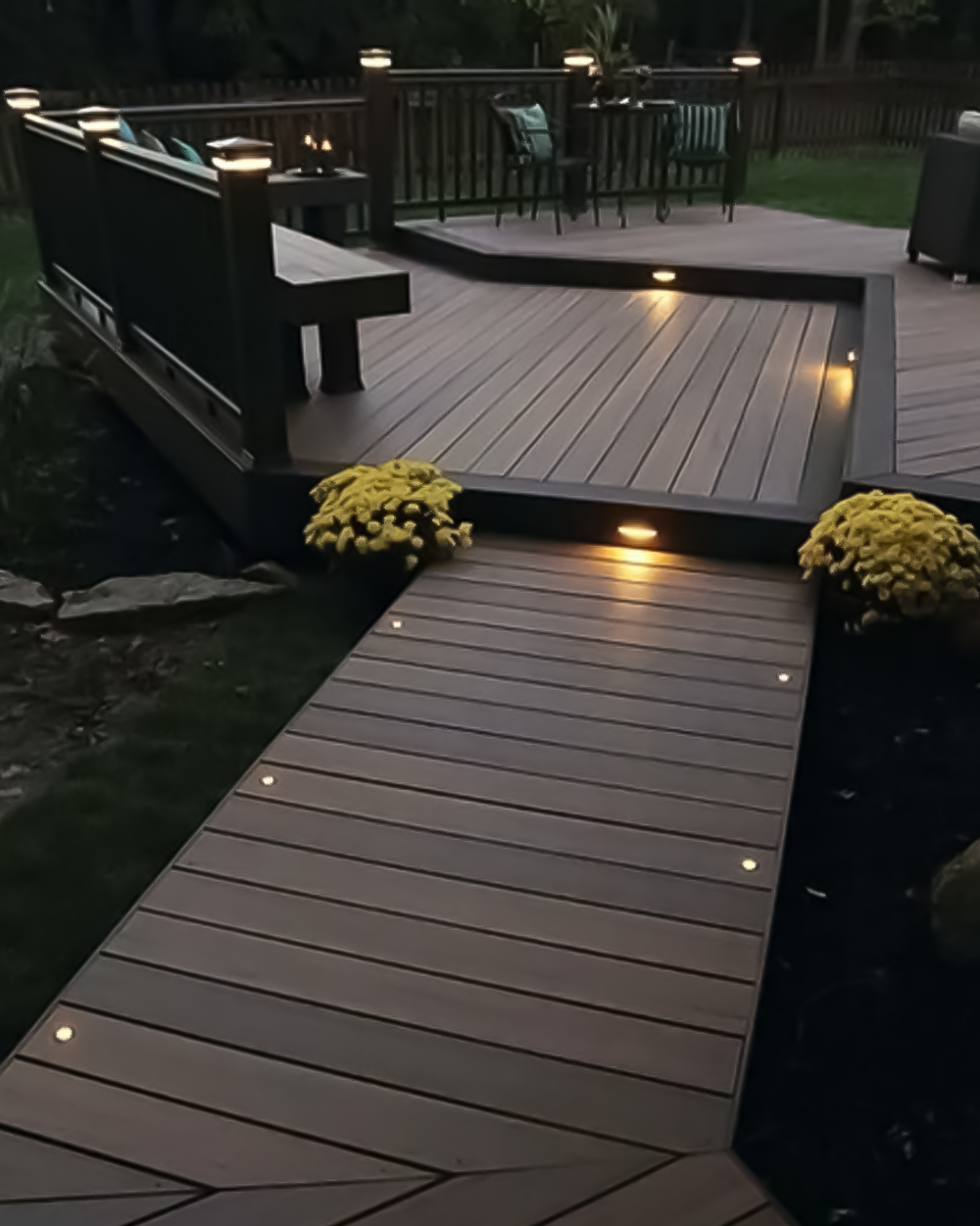 Terraza de madera con iluminación LED empotrada y barandales, ideal para jardín residencial.