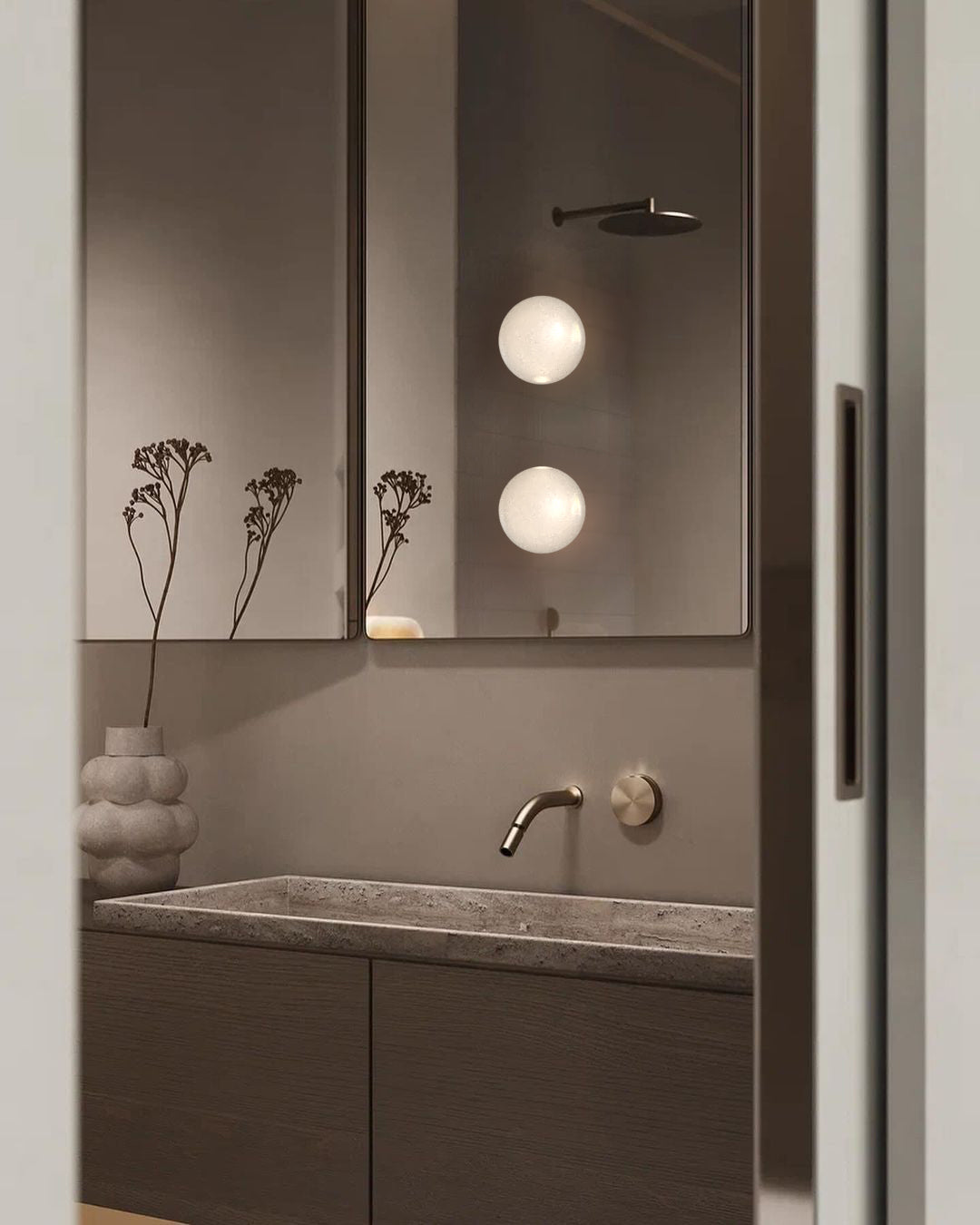 Baño moderno con lavabo de concreto, espejo grande y lámpara de pared esférica decorativa.