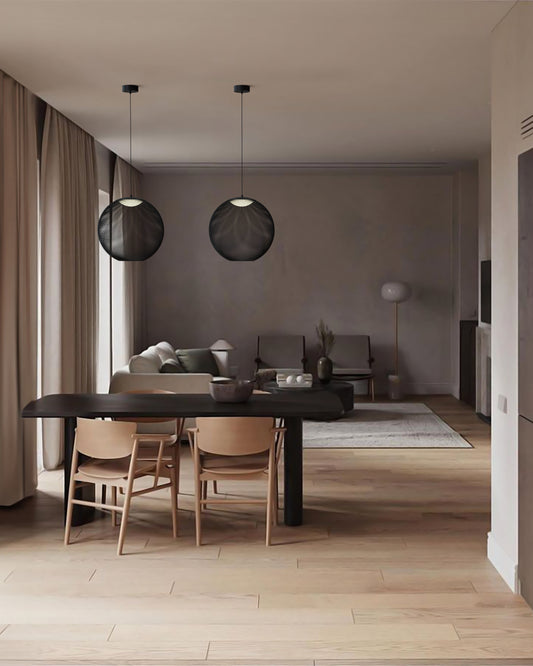 Lámparas colgantes modernas negras sobre comedor en sala minimalista con luz natural.