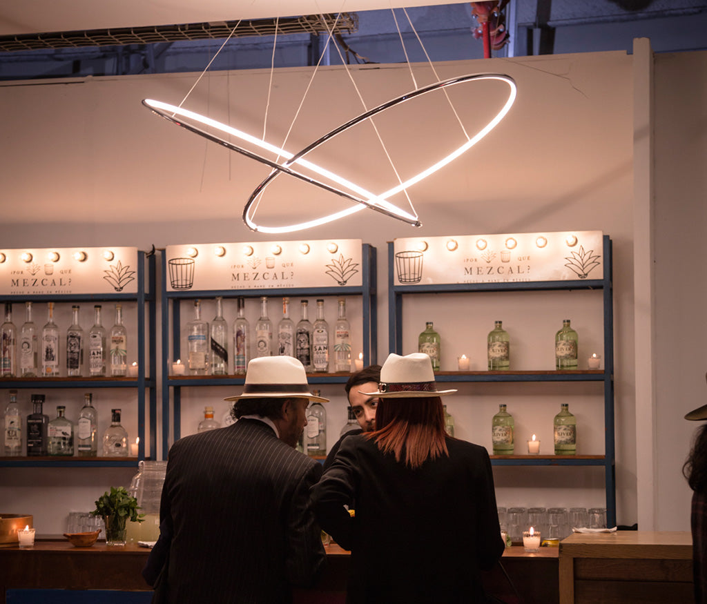 Lámpara colgante moderna de luz LED sobre barra de mezcal, con personas conversando