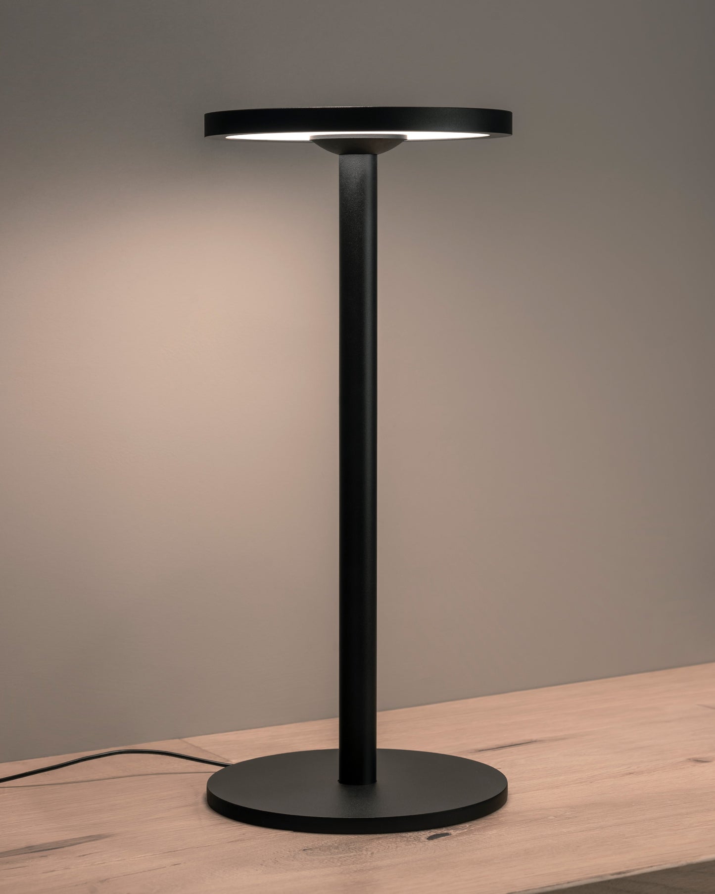 Lámpara de mesa negra moderna con base circular sobre superficie de madera, iluminación LED.
