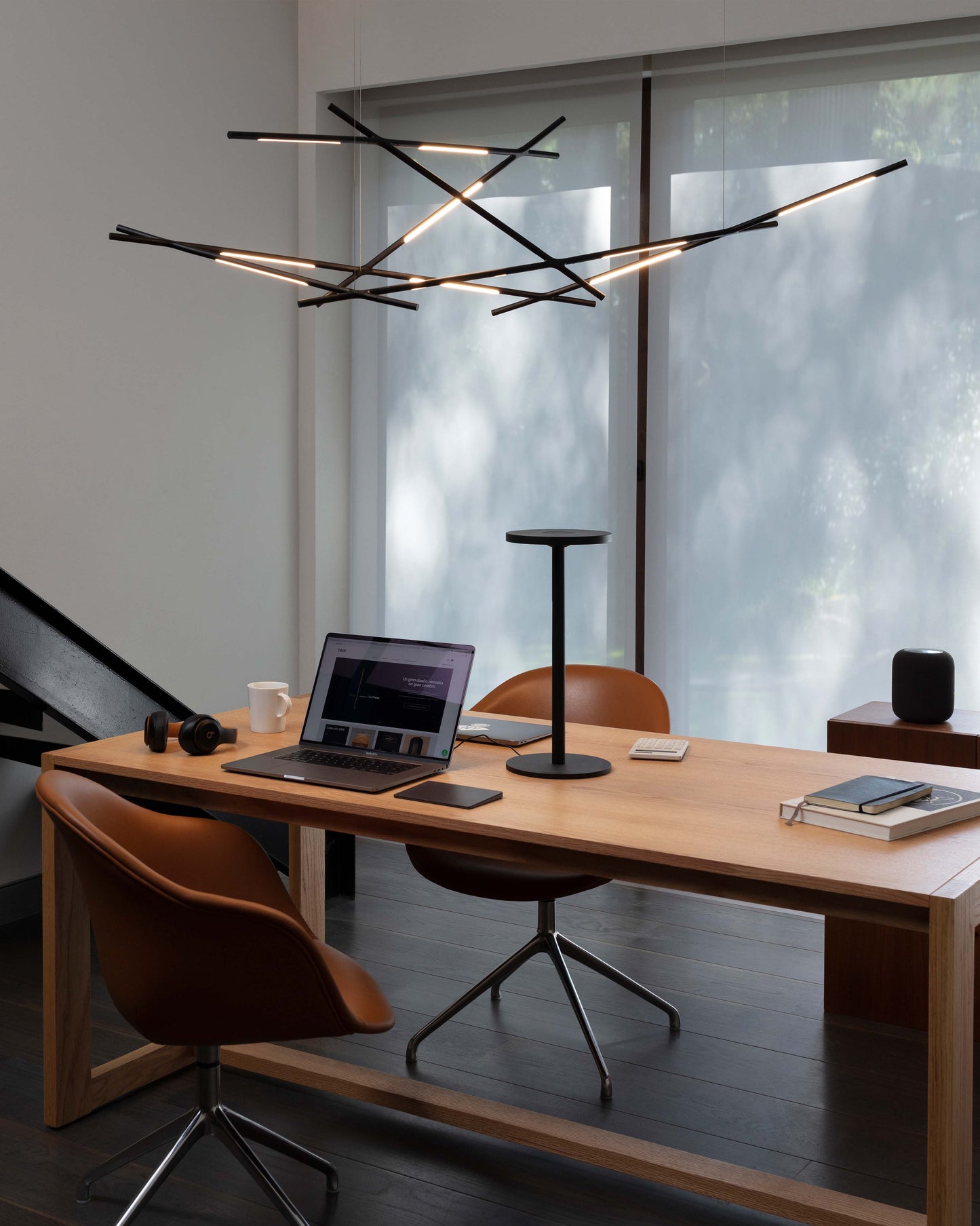 Lámpara de techo moderna de varillas LED negras en oficina minimalista con escritorio de madera.