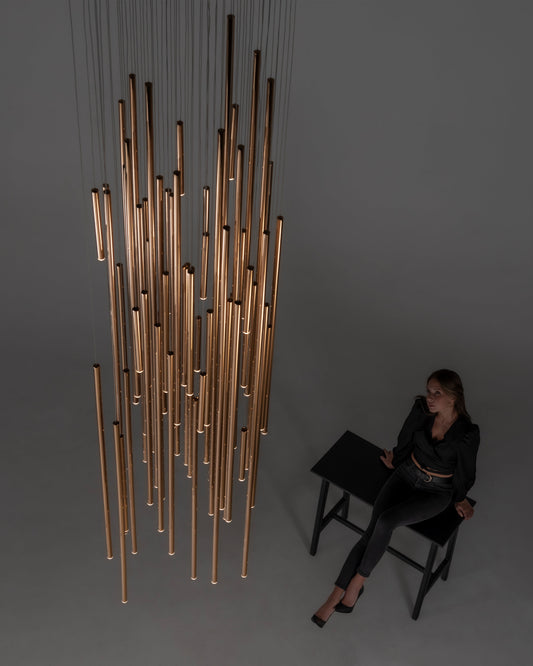 Lámpara colgante moderna de tubos dorados iluminados en interior minimalista con mujer sentada