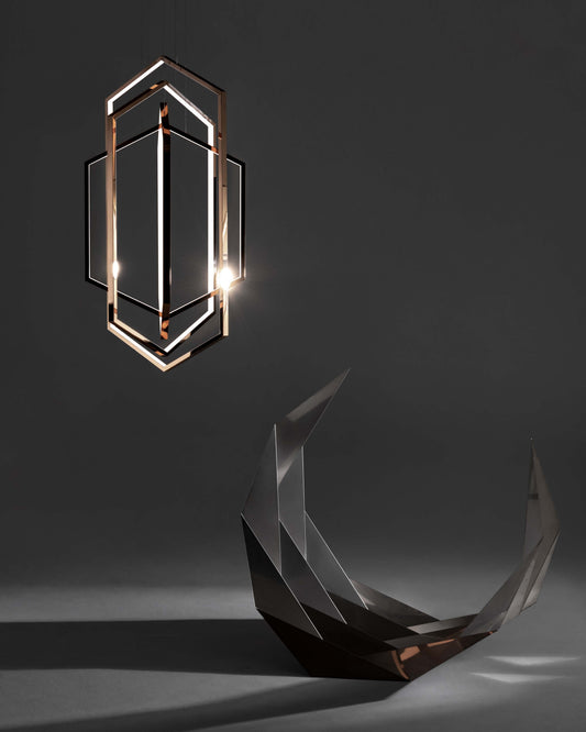Lámpara colgante moderna geométrica metálica iluminando escultura angular sobre fondo gris.