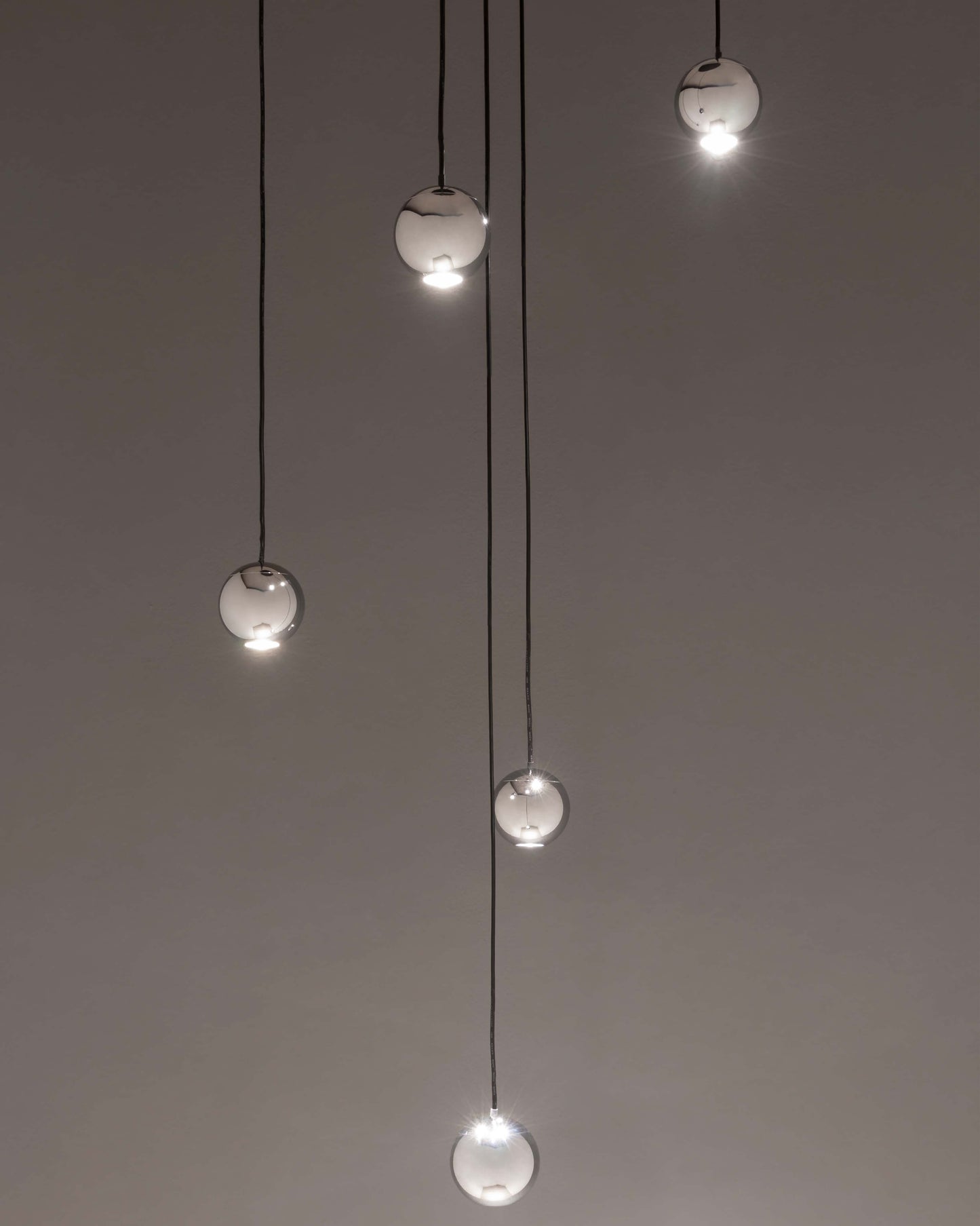 Lámparas colgantes esféricas de vidrio modernas encendidas sobre fondo gris minimalista.