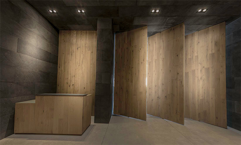 Recepción moderna con paneles de madera clara y paredes oscuras, iluminación empotrada LED.