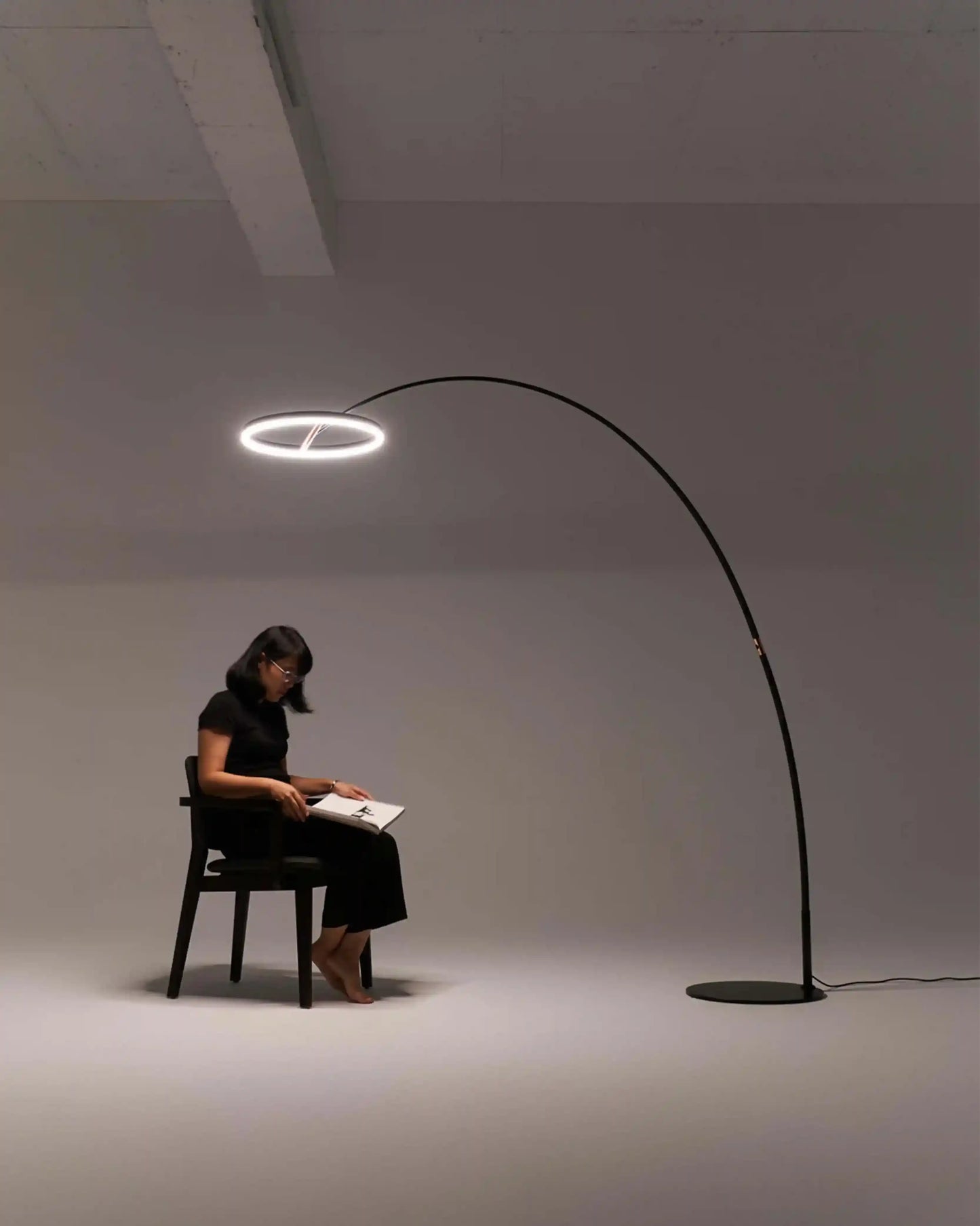 Lámpara de arco moderna iluminando a mujer sentada leyendo en estudio minimalista, Birot MX
