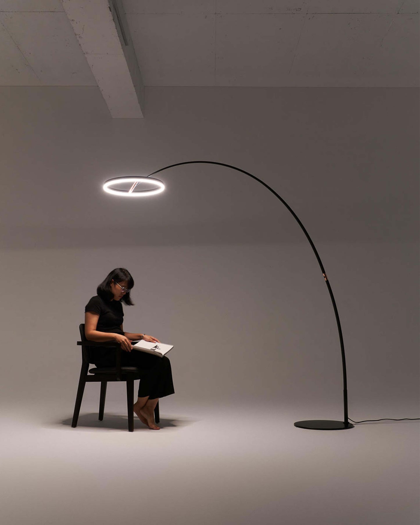 Lámpara de pie moderna con aro LED iluminando a mujer sentada leyendo en ambiente minimalista