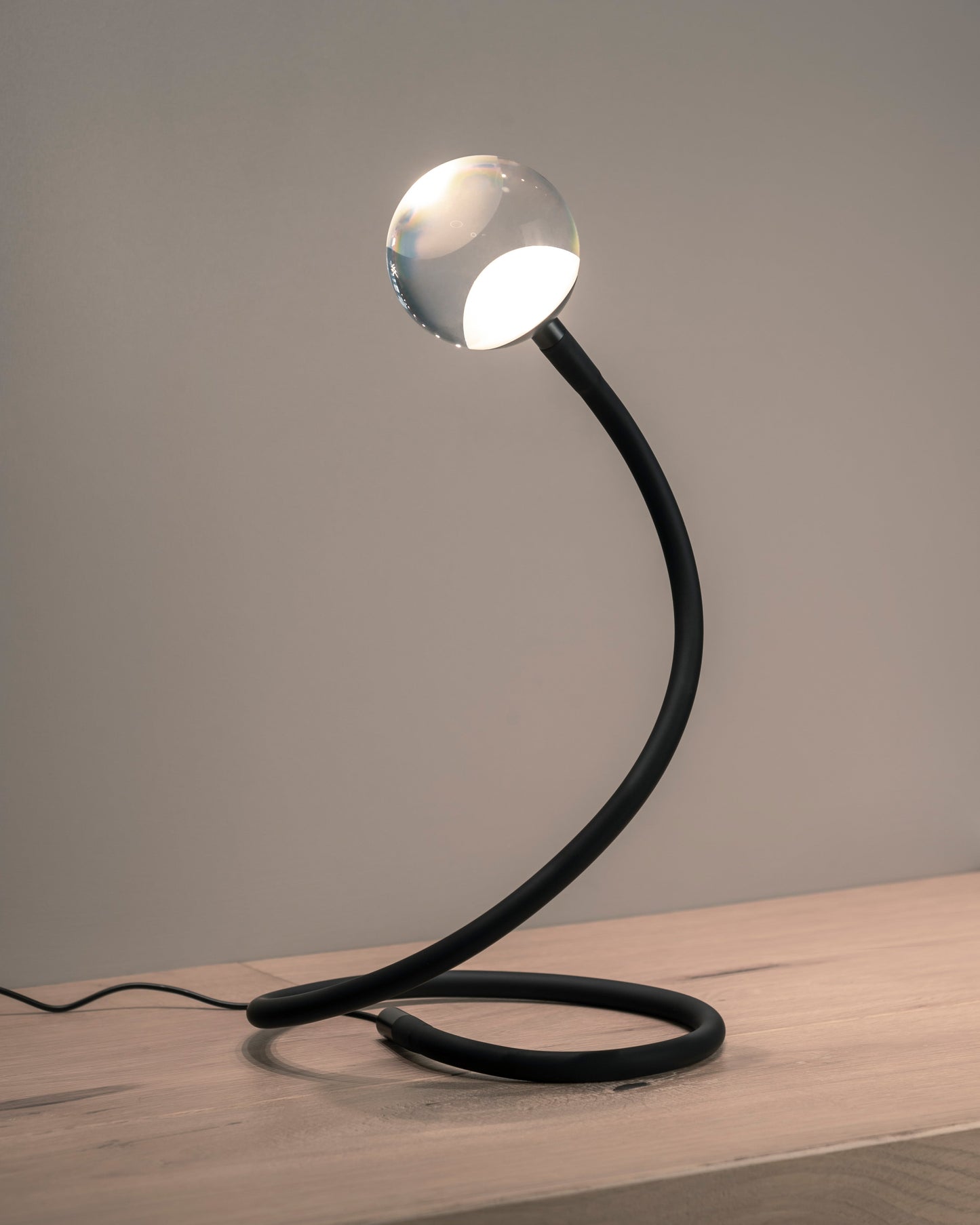 Lámpara de mesa moderna con base curva negra y esfera de cristal, iluminación decorativa.