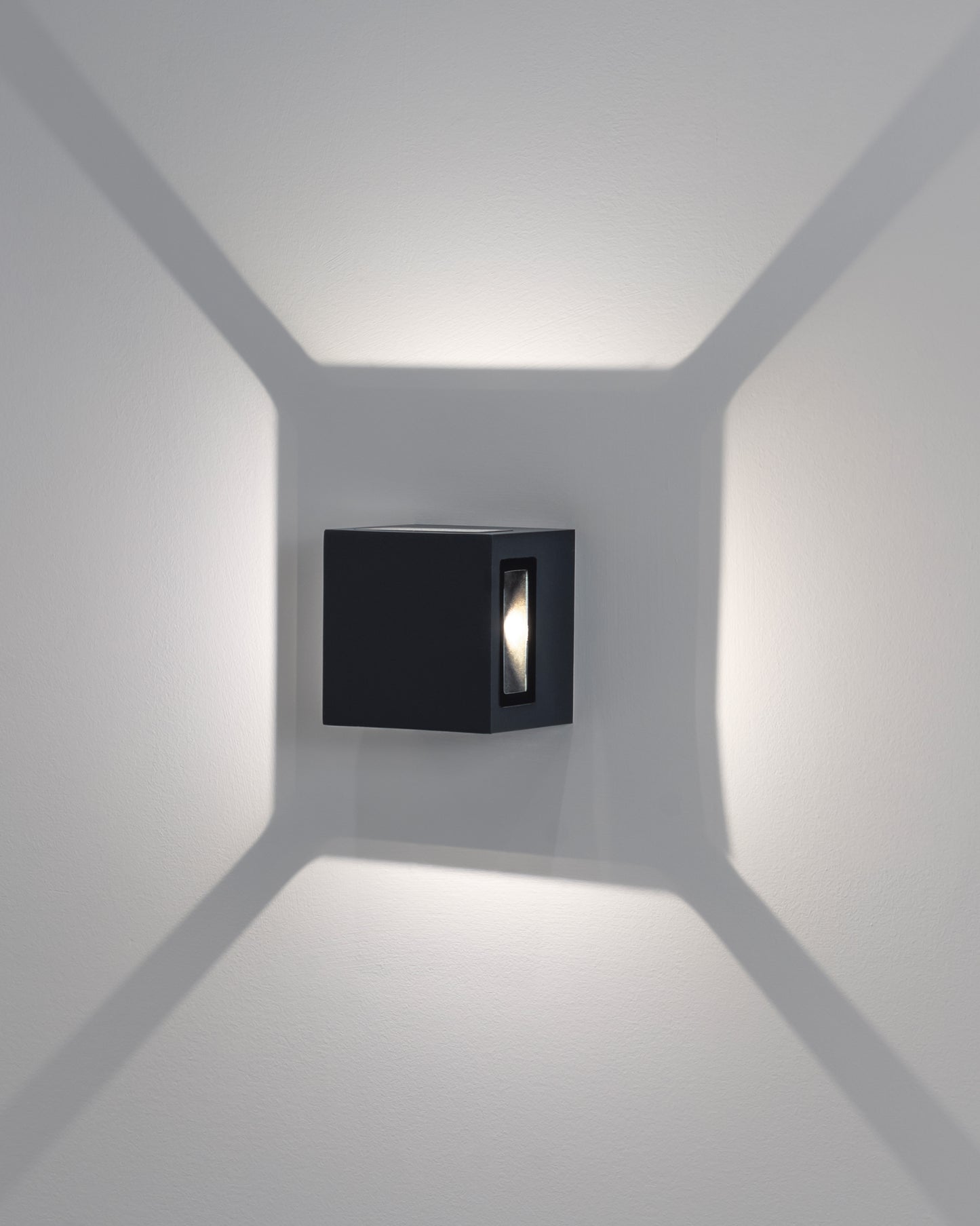 Aplique de pared moderno negro con luz LED proyectando patrones geométricos en la pared.