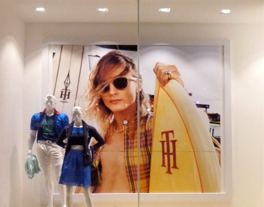 Escaparate con maniquíes y fondo de cartel publicitario de surfista con tabla, iluminación de boutique.