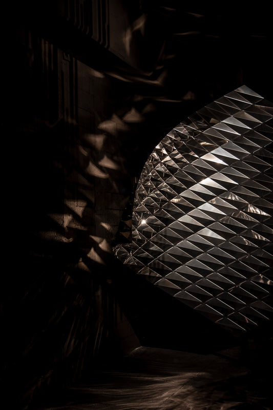 Lámpara decorativa metálica con patrón geométrico, crea efectos de luz y sombra artística.