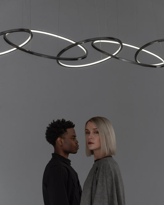 Lámpara colgante moderna de aros LED negros sobre dos personas en espacio minimalista.