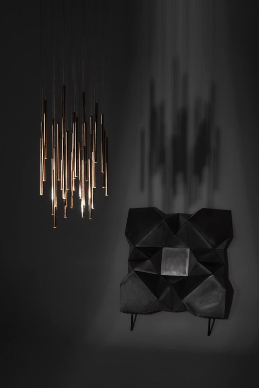 Lámpara colgante moderna de tubos dorados junto a sillón geométrico negro en ambiente minimalista
