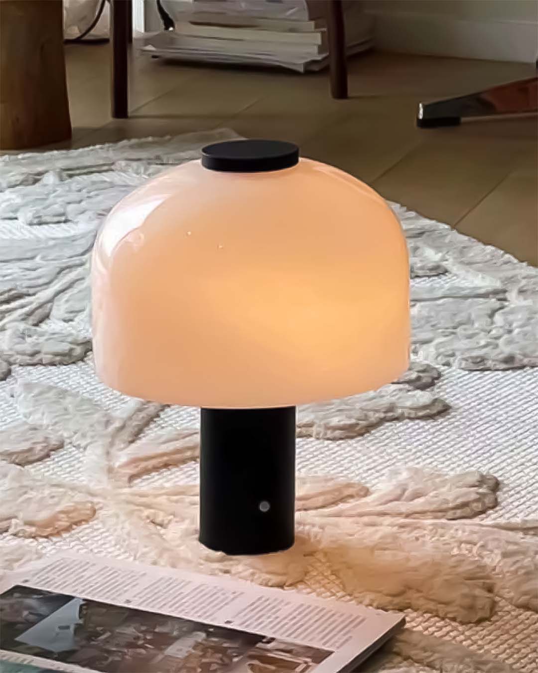 Lámpara de mesa moderna con base negra y pantalla opalina, sobre alfombra en sala de estar
