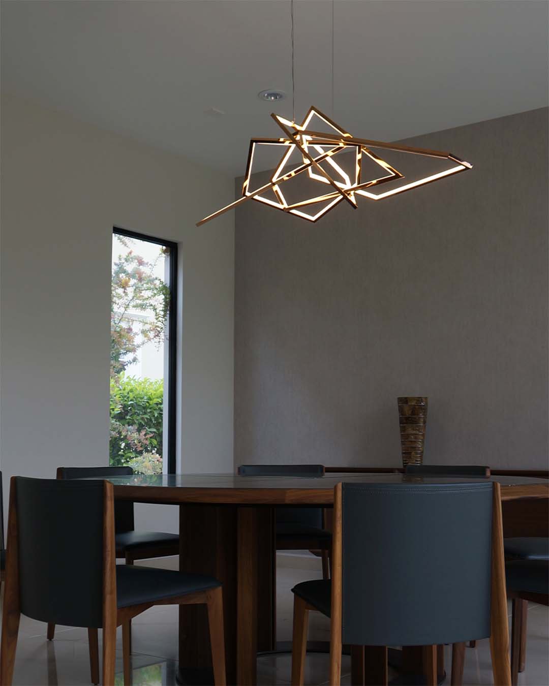 Lámpara colgante moderna geométrica iluminando comedor minimalista con mesa y sillas de madera.
