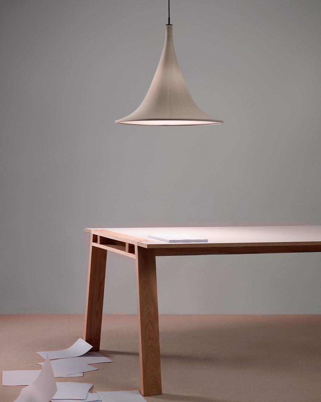 Lámpara colgante moderna sobre mesa de madera, papeles en el suelo, iluminación Birot MX