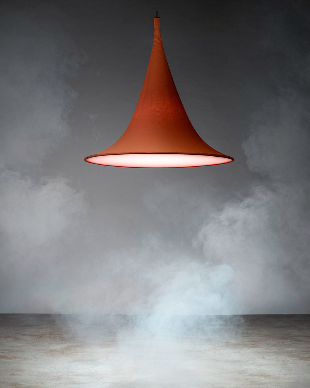 Lámpara colgante moderna color terracota encendida, fondo con humo y ambiente minimalista.