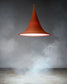 Lámpara colgante moderna color terracota encendida, fondo con humo y ambiente minimalista.