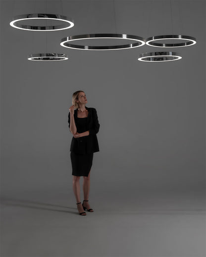 Lámparas colgantes LED circulares modernas en techo gris, mujer de pie debajo.