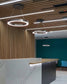 Lámparas circulares LED colgantes en oficina moderna con techo de madera y recepción de mármol.