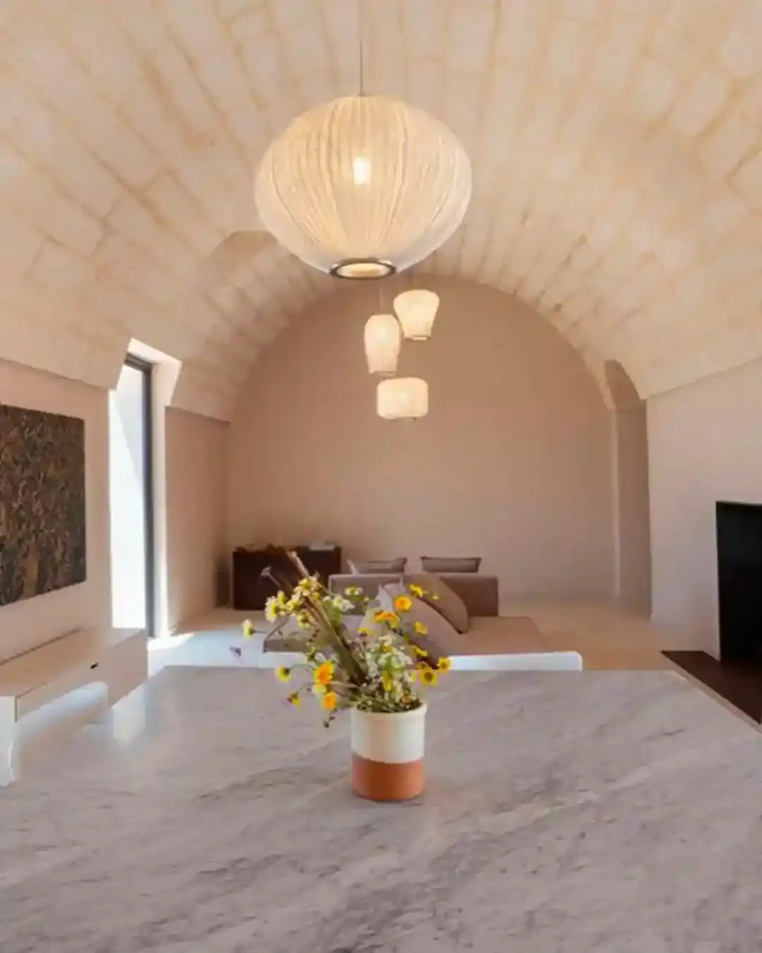 Lámparas colgantes de diseño en sala moderna con mesa de mármol y flores, Birot MX iluminación.