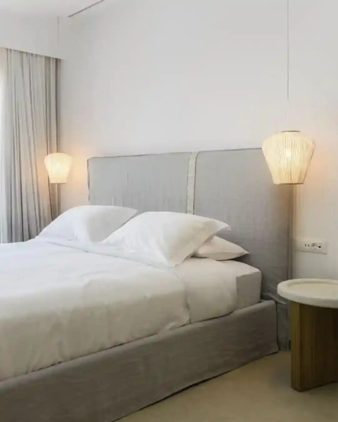 Dormitorio moderno con lámparas colgantes de Birot MX y cama con ropa de cama blanca.