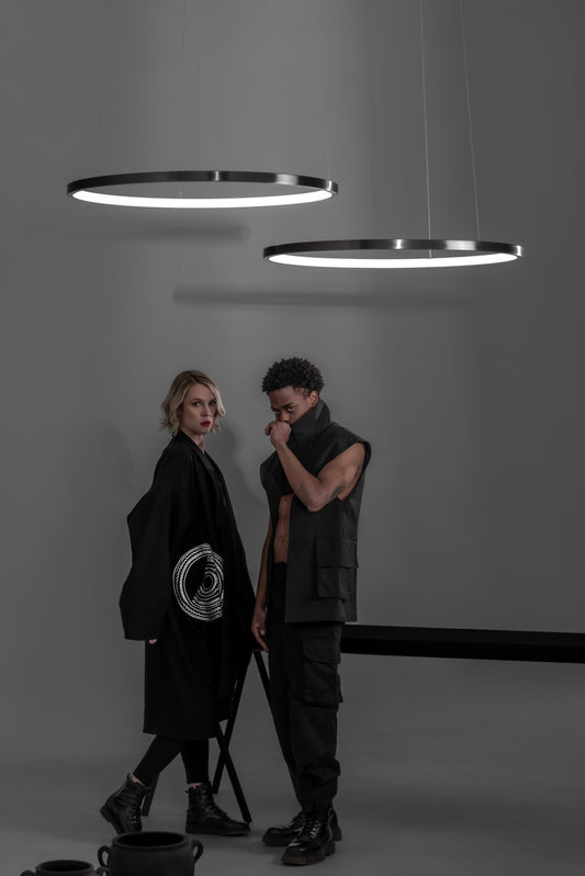 Lámparas colgantes LED modernas sobre dos personas con ropa negra en fondo minimalista.