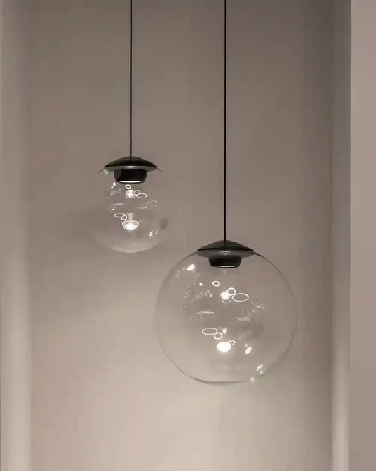 Lámparas colgantes de vidrio esférico iluminando pared blanca, boutique de iluminación Birot MX.