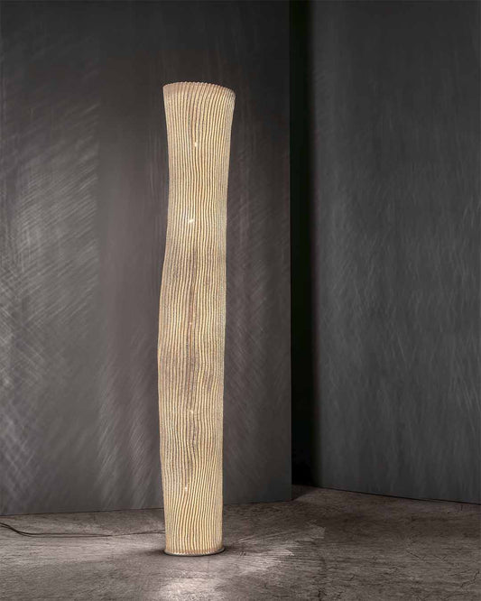 Lámpara de pie diseño escultural Gea, en malla de acero inox plegada, ambiente con luz cálida. 