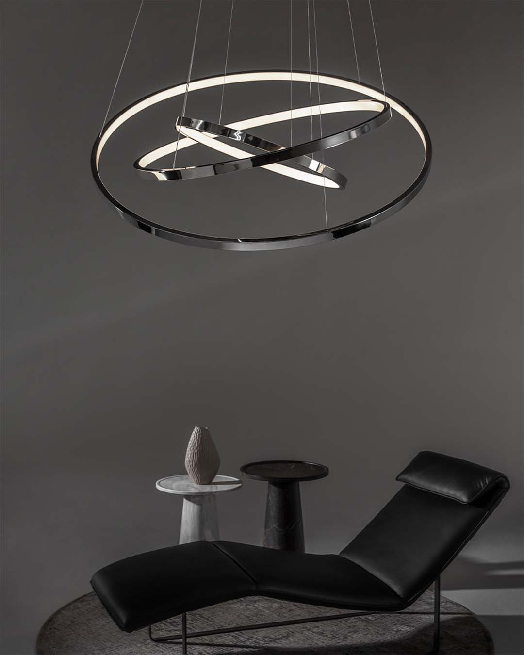 Lámpara colgante LED moderna circular en sala minimalista con sillón negro y mesas auxiliares.