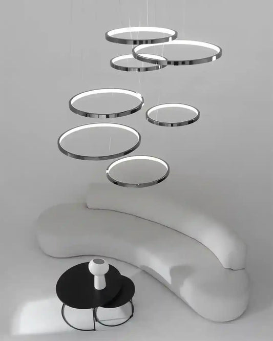 Lámpara colgante de anillos LED modernos sobre sofá curvo blanco y mesa negra en sala minimalista