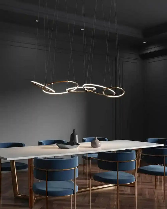 Lámpara colgante dorada moderna sobre mesa blanca y sillas azules en comedor elegante, Birot MX boutique de iluminación.