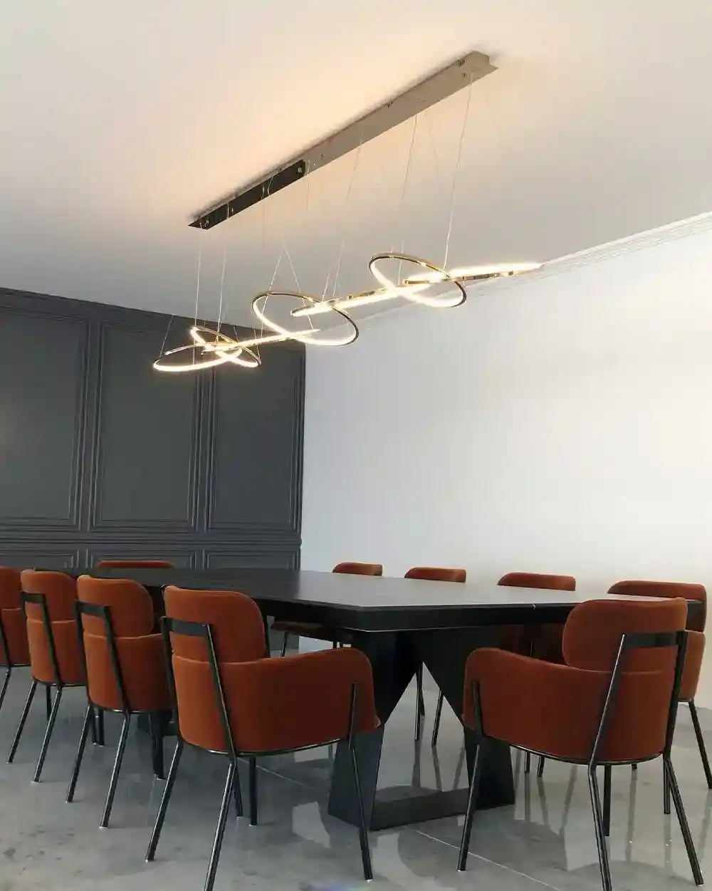 Lámpara colgante moderna sobre mesa negra y sillas naranjas en comedor elegante, Birot MX.
