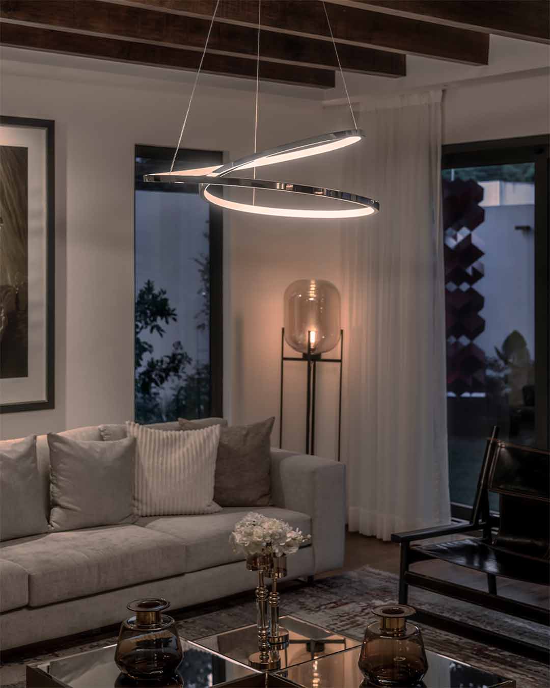 Lámpara colgante moderna de anillos LED iluminando sala de estar elegante con sofá gris.