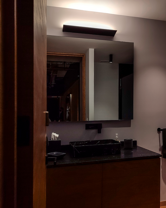 Baño moderno con lavabo negro de mármol, espejo grande y luz LED decorativa en la pared.