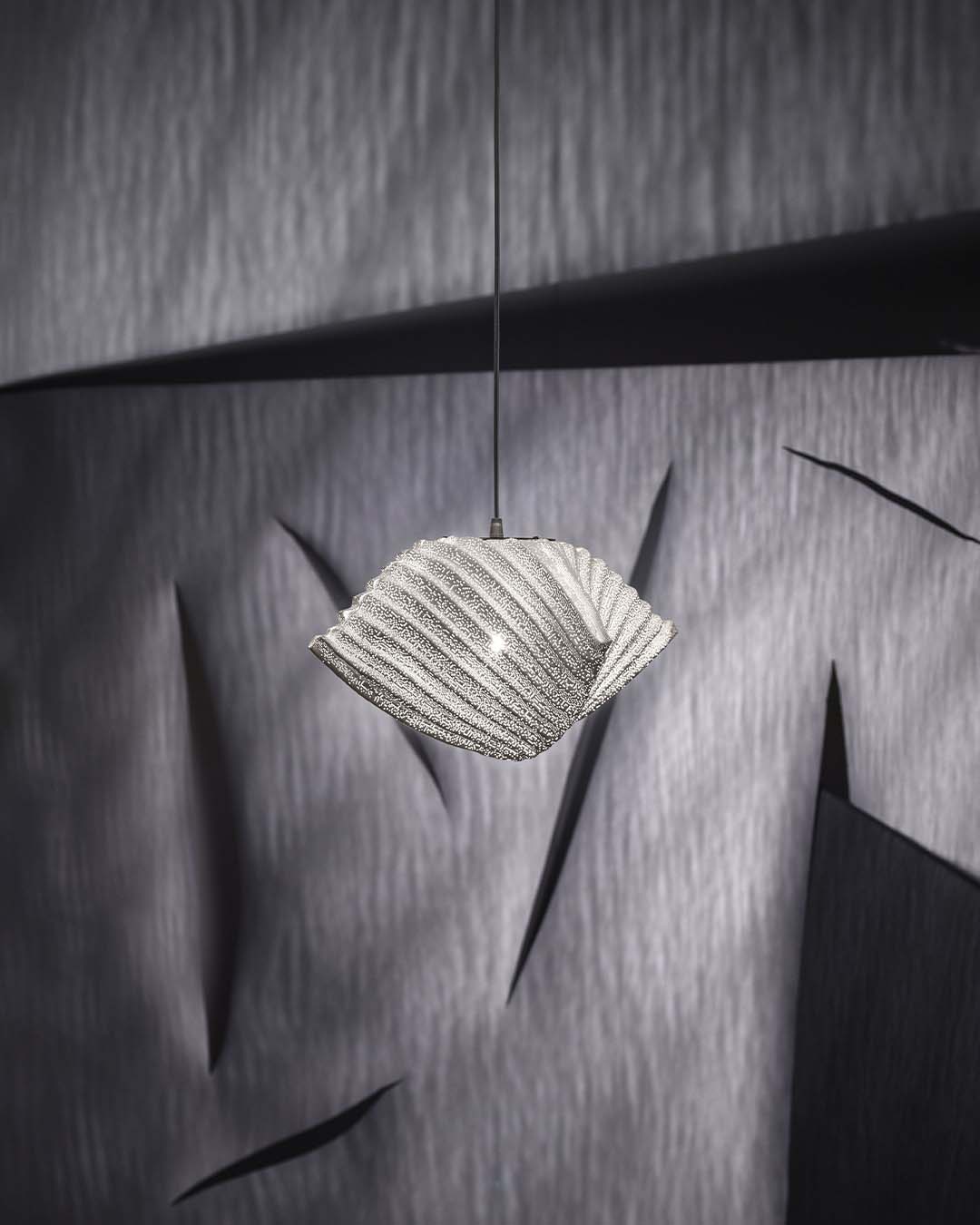 Lámpara colgante moderna de cristal en ambiente minimalista con fondo texturizado gris.