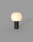 Luminaria de mesa portátil LED Liora en base negra y pantalla opalina encendida.