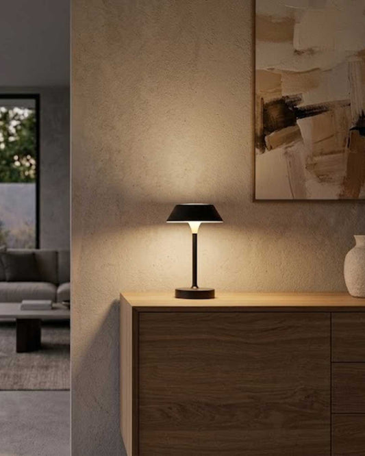 Lámpara de mesa portátil Metu en acabado negro con luz LED encendida sobre credenza de madera.