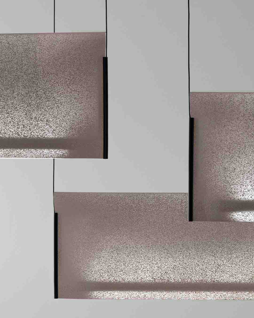 Lámparas colgantes modernas de paneles rectangulares color rosa metálico, fondo gris claro.