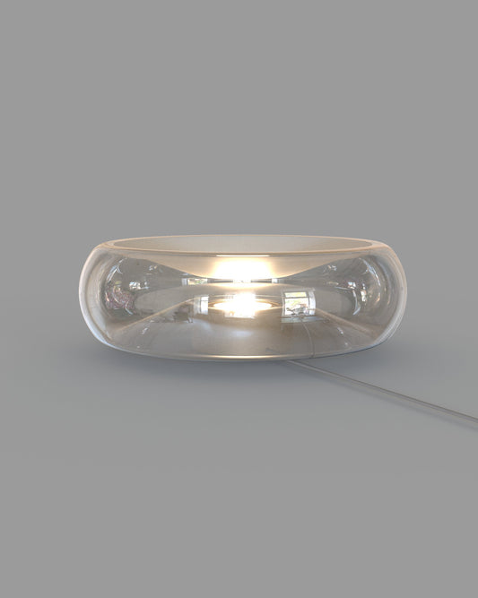 Lámpara de mesa moderna de vidrio transparente con luz cálida encendida, fondo gris.