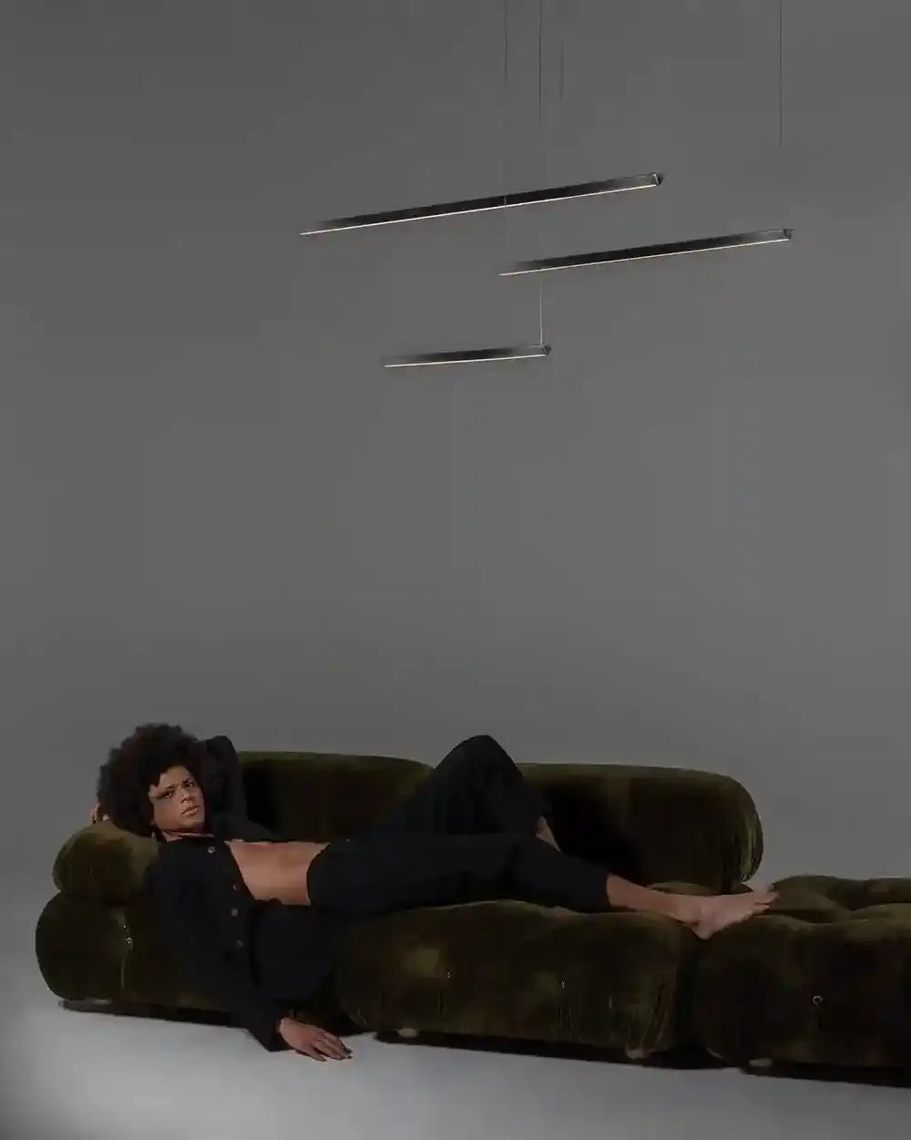 Lámparas colgantes modernas de línea fina sobre sofá aterciopelado en sala minimalista.