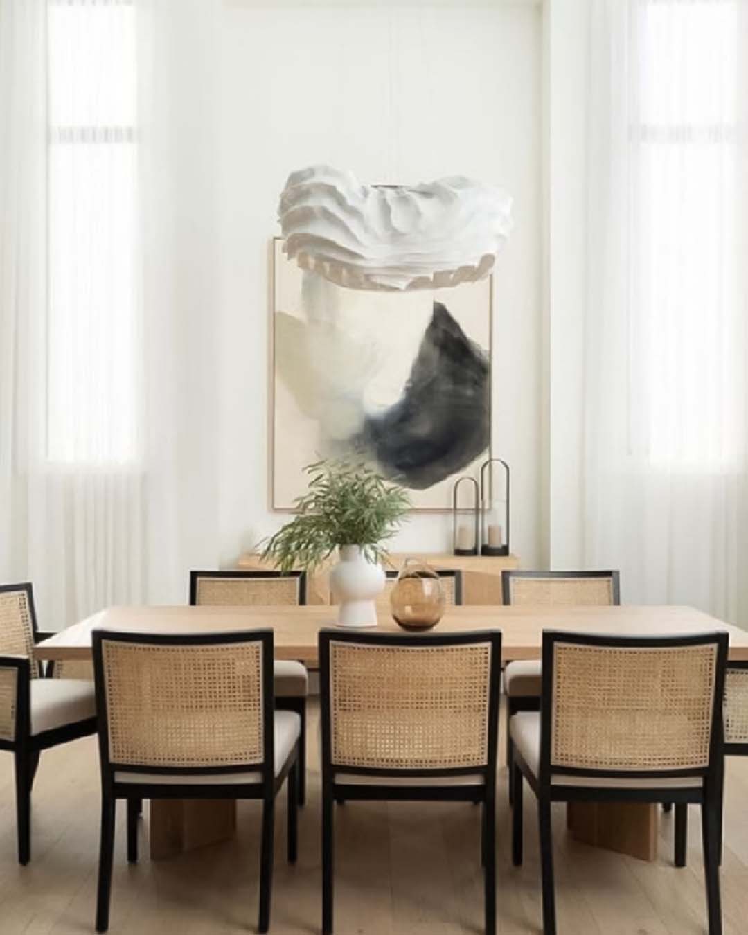 Comedor moderno con lámpara escultórica blanca, cuadro abstracto y sillas de mimbre, iluminación Birot MX.
