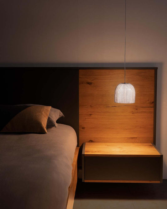 Lámpara colgante moderna iluminando mesa de noche y cabecera de madera en dormitorio